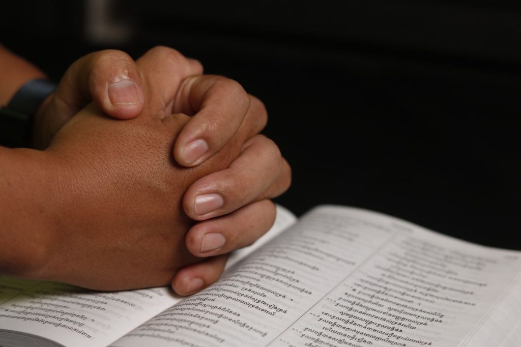 Hands folded in prayer over an open Bible.